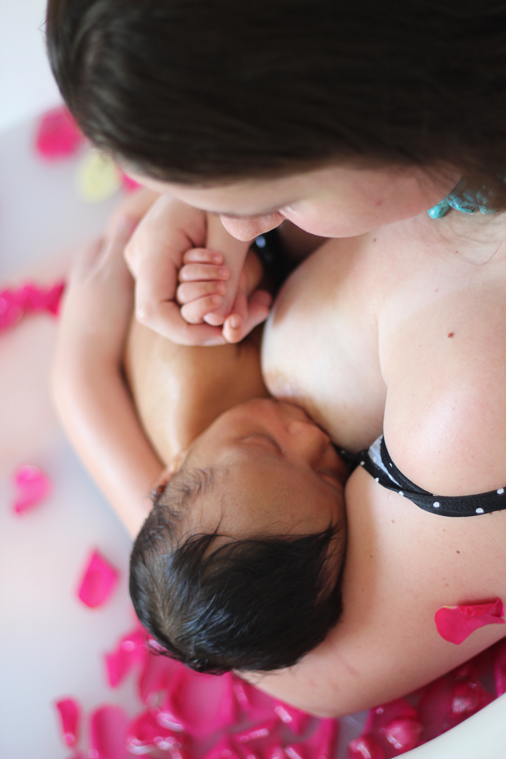 Mother breastfeeding her baby in a milk bath with rose petals.